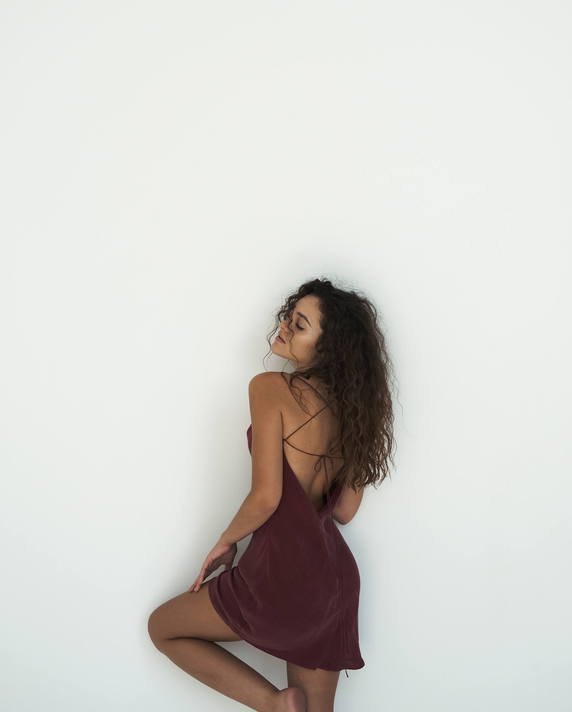 Woman in a burgundy slip dress against a white background