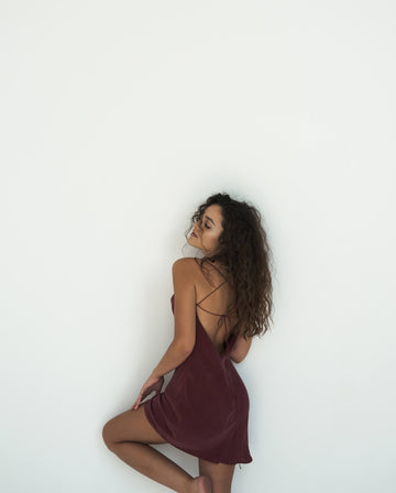 Woman in a burgundy slip dress against a white background
