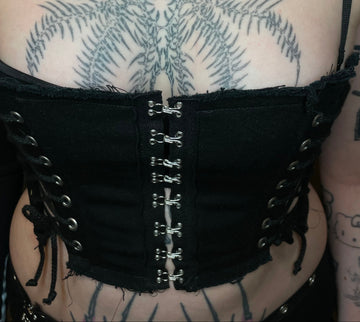 Black lace-up garment with metal hooks on a tattooed arm