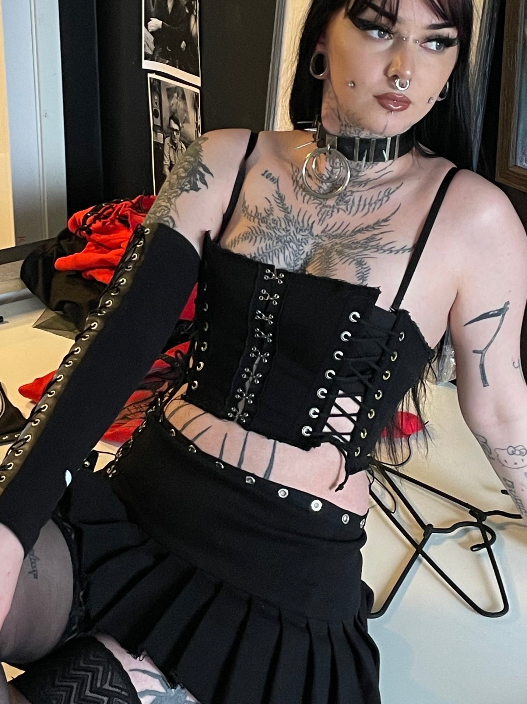 Person wearing corset and grunge mini skirt sitting on a chair in a room with artwork on the wall.