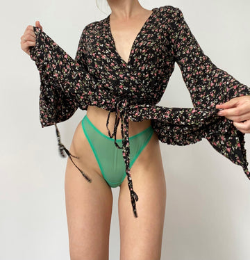 Person wearing a floral long-sleeve top and green bikini bottoms on a plain background