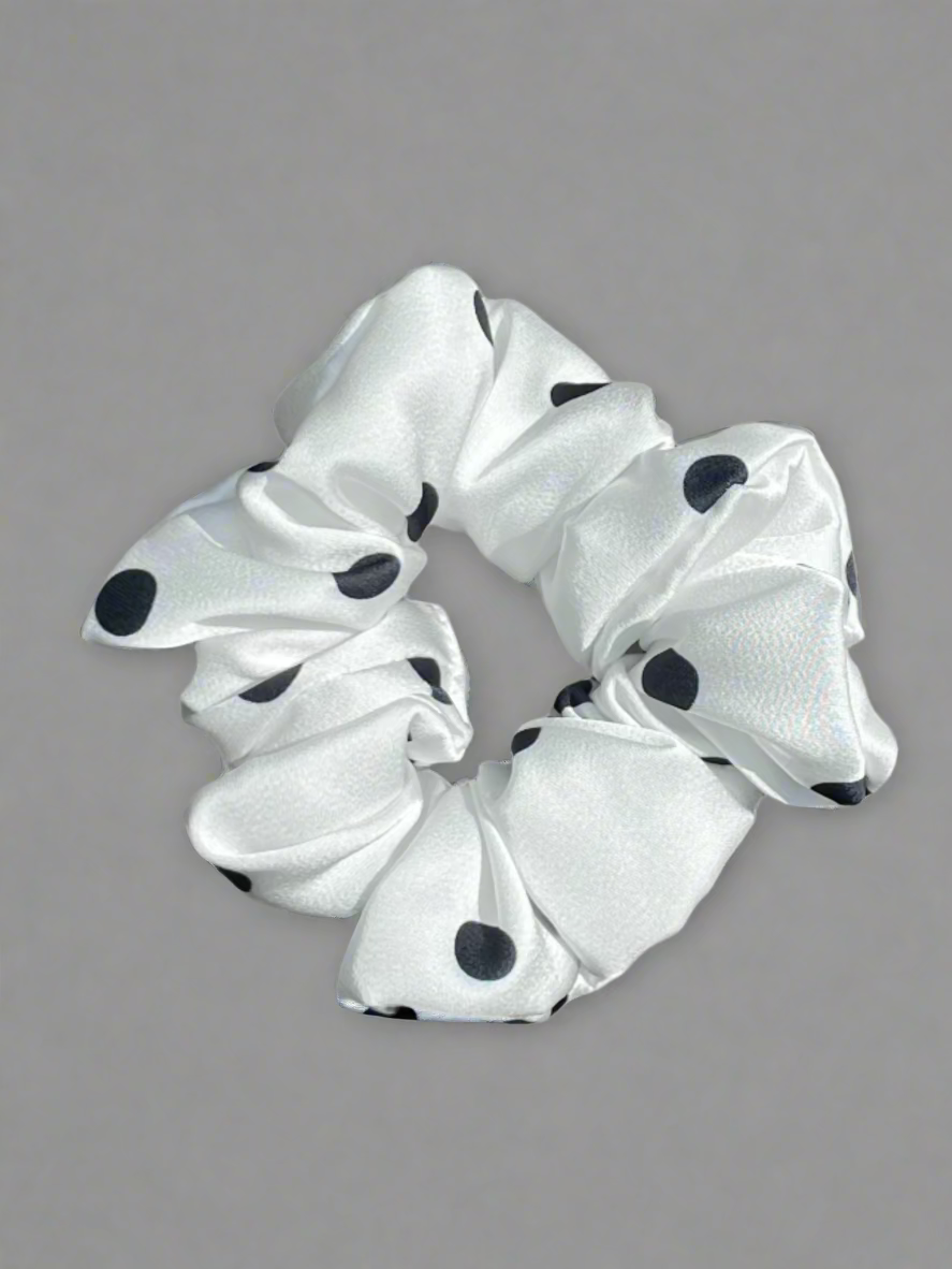 White scrunchie with black polka dots on a wooden surface