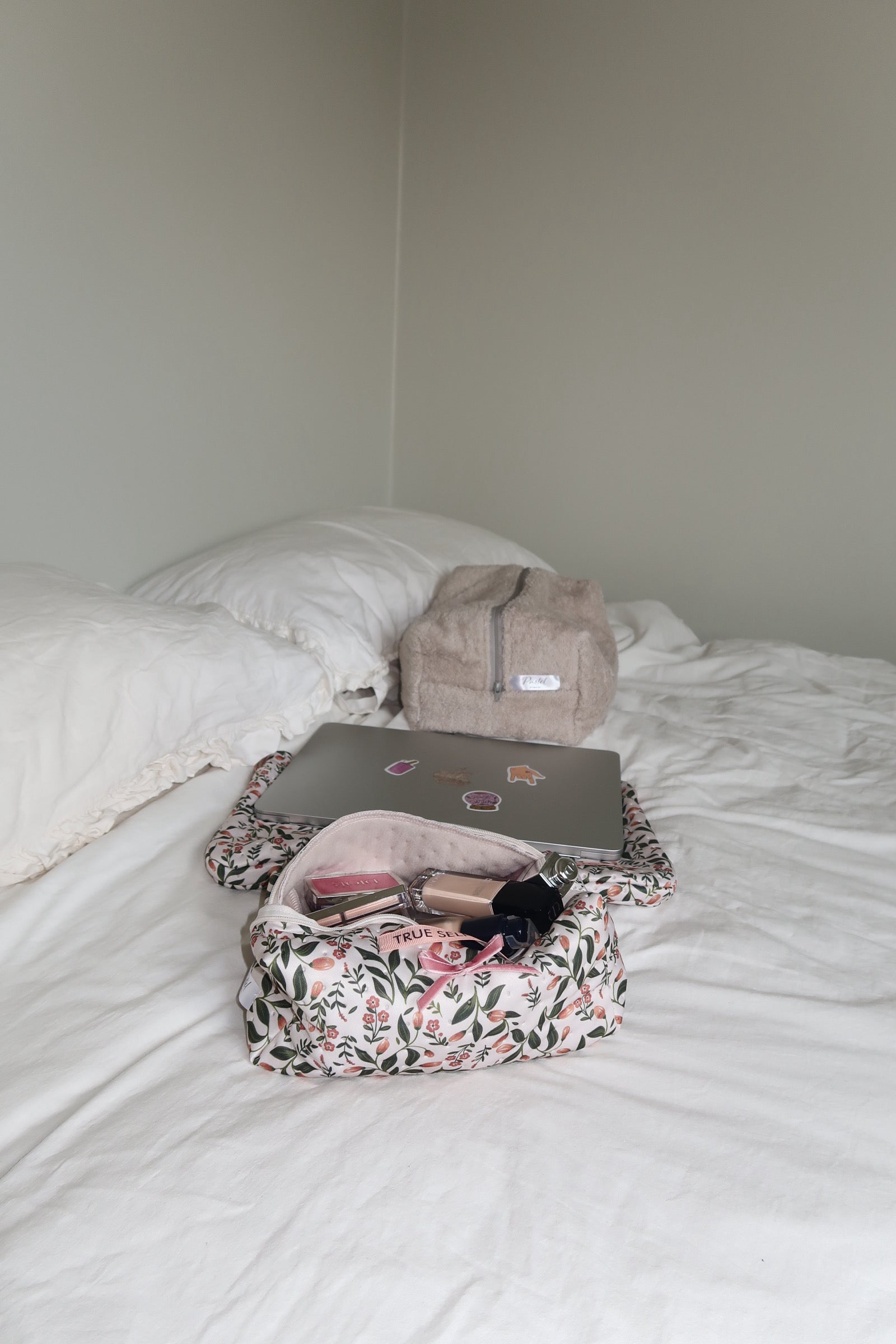 Small backpacks and a floral bag on a white bed